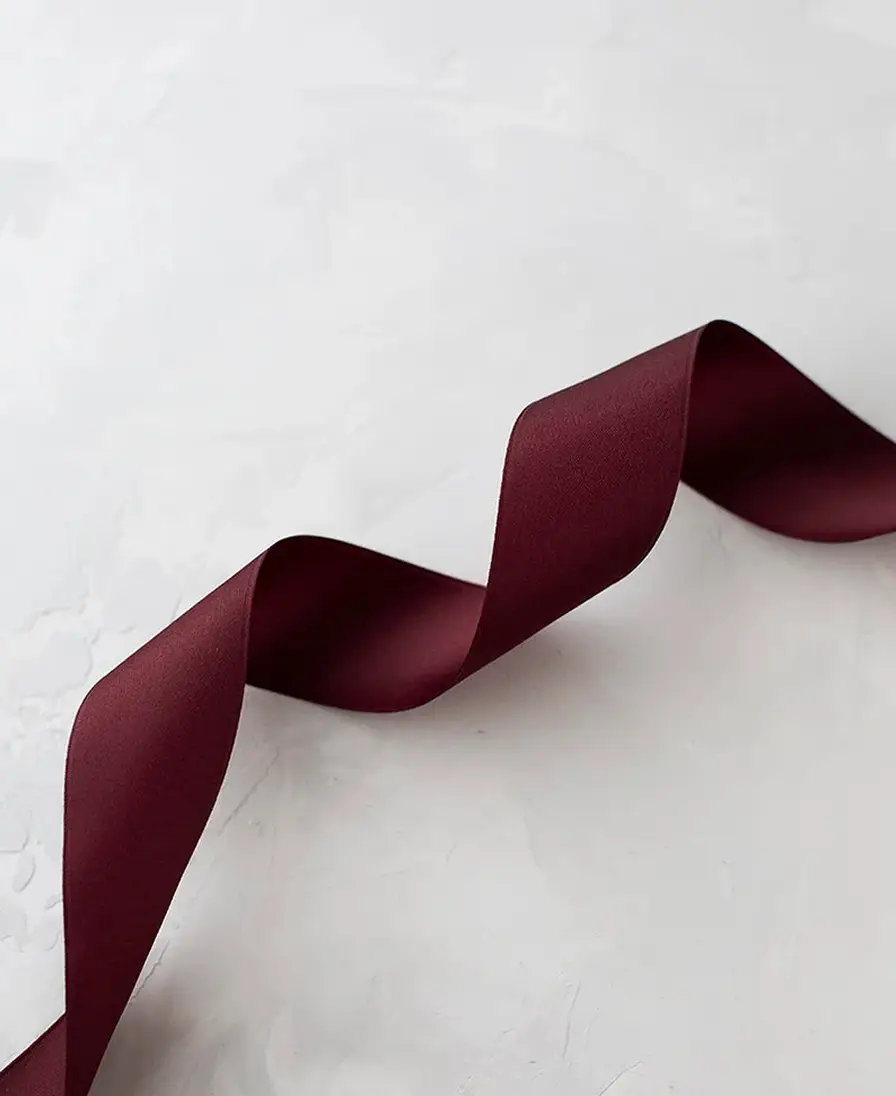 Ribbons Curled burgundy satin ribbon on a textured grey surface.