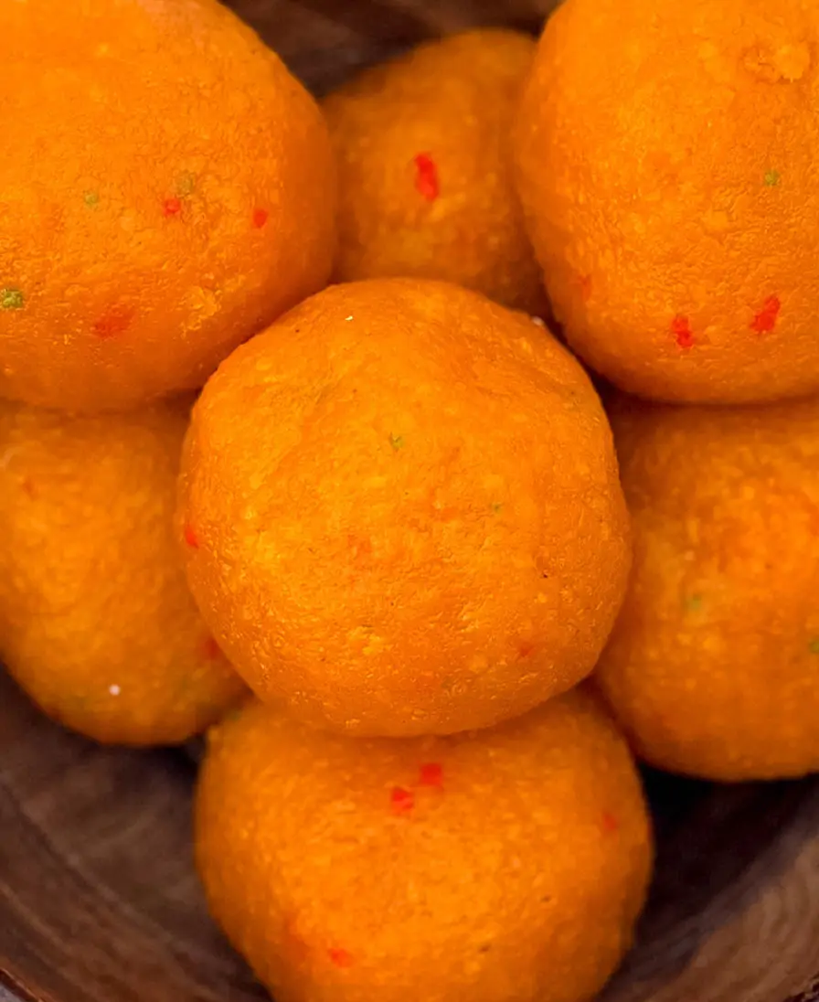 Classic motichoor ladoo Close-up of handmade orange motichoor ladoo, fine-grained and flecked with red and green, in a wooden bowl.