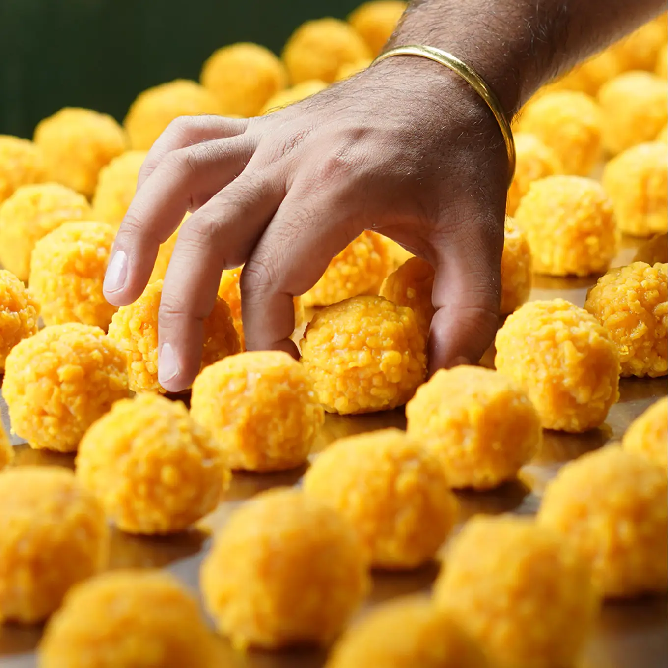 Hand-rolled boondi ladoo Hand reaching for freshly rolled golden boondi ladoo arranged in rows on a tray.