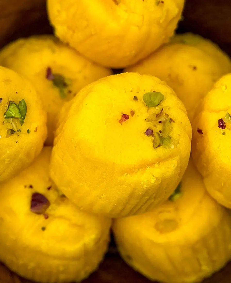Kesar peda Close-up of handmade saffron-gold kesar peda finished with pistachio, in a wooden bowl.
